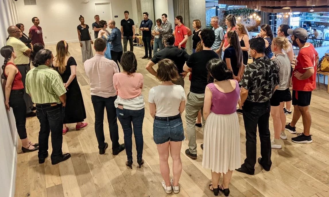 A summer class circle of students gathered on a wooden studio floor