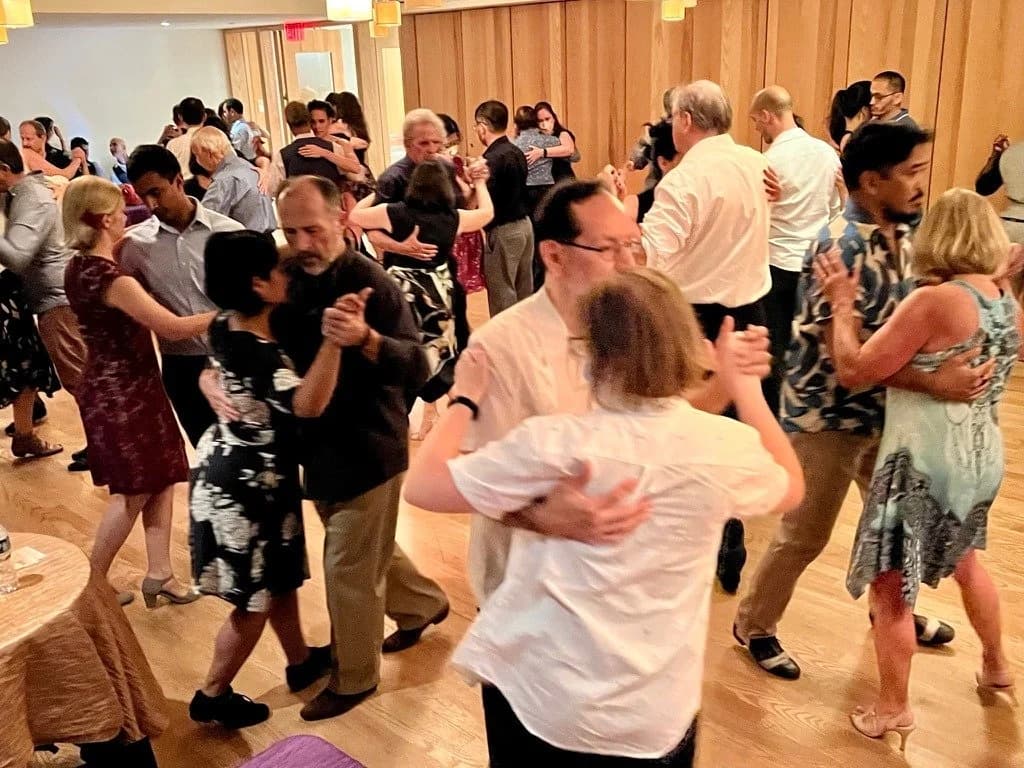 Couples in close embrace on a crowded First Saturday milonga floor